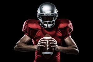 Football player in uniform against black background.
